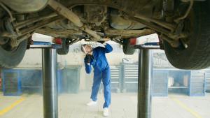 Mechanic inspecting vehicle's undercarriage in an auto repair shop, emphasizing frame damage and structural integrity for safety after collisions.