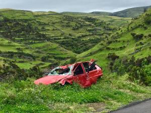 Damaged red car abandoned in lush green landscape, illustrating the dangers of frame damage and the importance of professional repair services at 360 Collision.