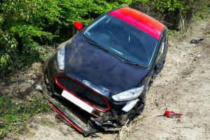 Damaged black and red car in a ditch, illustrating frame distortion and potential safety risks related to vehicle accidents and misalignment.