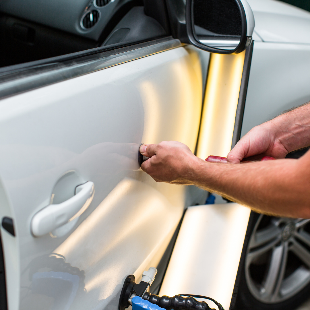Hands using tools for Paintless Dent Repair on a white car door, showcasing the repair process with specialized equipment and lighting.