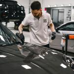Auto body technician performing repair work on a black car hood in a San Antonio collision repair shop.