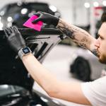Auto body technician applying a pink squeegee on a vehicle's hood in a professional repair shop, highlighting skilled labor in collision repair.