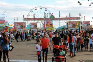 Crowd enjoying the San Antonio Stock Show & Rodeo, featuring families, carnival rides, and festive booths.