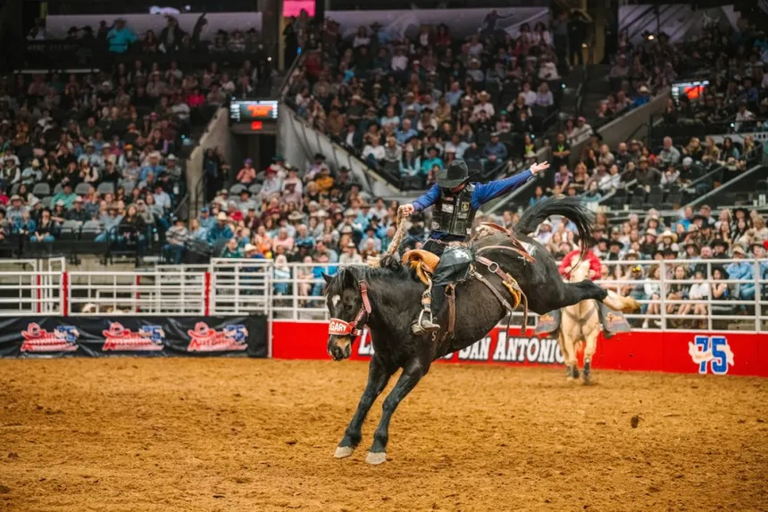 Rodeo cowboy riding a bucking horse in San Antonio arena, surrounded by a cheering crowd, highlighting the excitement of the San Antonio Stock Show & Rodeo.